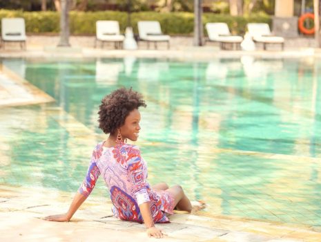 Founder Rosetta Thurman sitting at the edge of a pool wearing a pink patterned dress with her hair in a textured afro